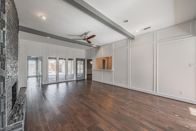 unfurnished living room featuring ceiling fan, dark hardwood / wood-style floors, a fireplace, and beam ceiling