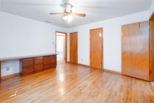 unfurnished bedroom with light hardwood / wood-style flooring, two closets, built in desk, and ceiling fan