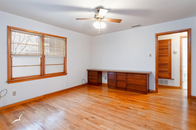 empty room with built in desk, ceiling fan, and light wood-type flooring