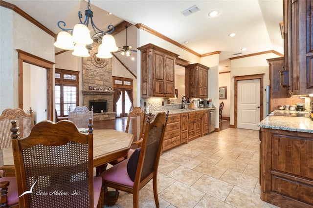 dining area with crown molding, sink, a stone fireplace, and ceiling fan with notable chandelier