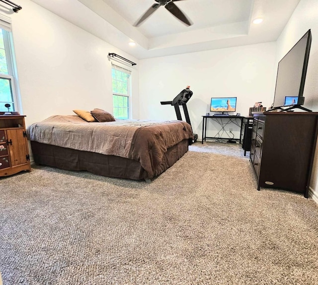 carpeted bedroom with ceiling fan and a tray ceiling