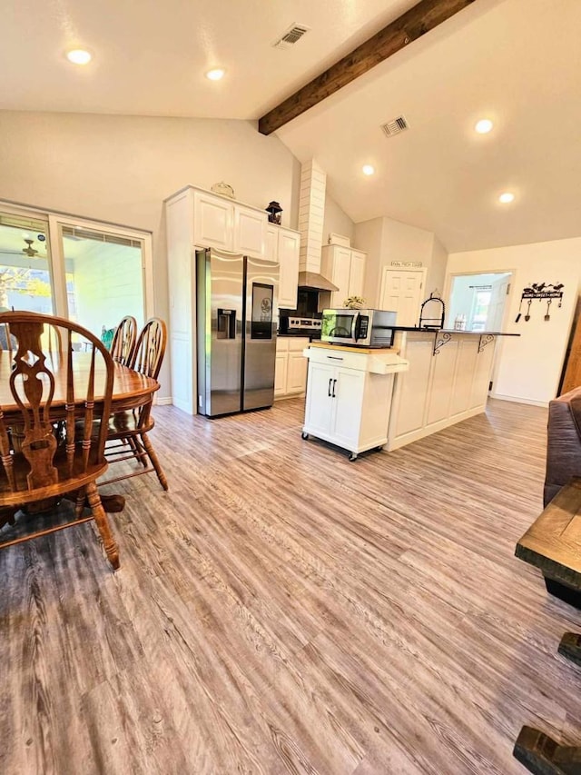 kitchen with stainless steel appliances, vaulted ceiling with beams, white cabinets, and light hardwood / wood-style floors