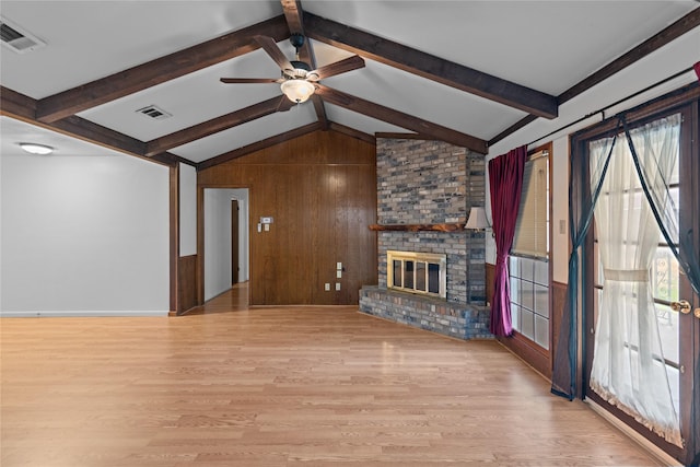 unfurnished living room featuring wooden walls, a brick fireplace, light hardwood / wood-style flooring, and vaulted ceiling with beams