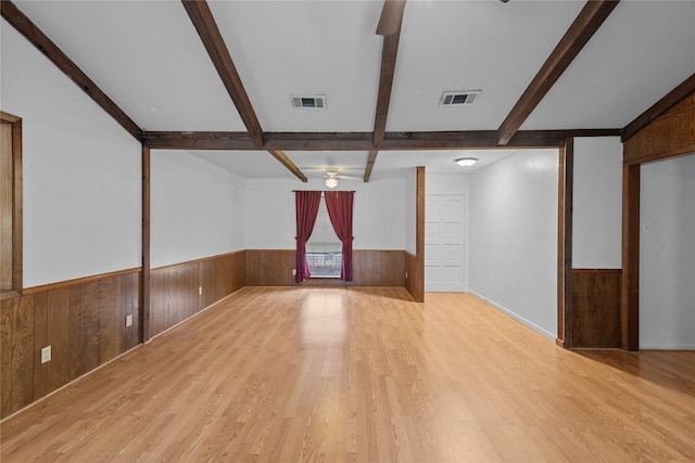 unfurnished living room with ceiling fan, wooden walls, beamed ceiling, and light wood-type flooring