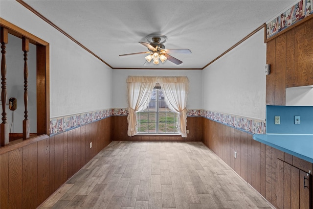 empty room with wood walls, a textured ceiling, light hardwood / wood-style flooring, ornamental molding, and ceiling fan