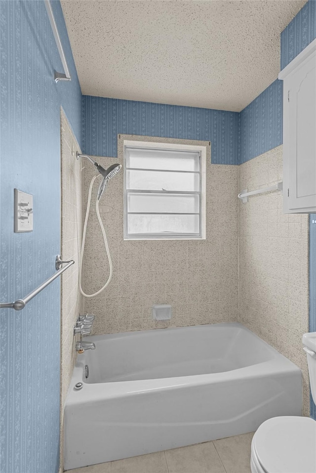 bathroom featuring tiled shower / bath, toilet, tile patterned flooring, and a textured ceiling