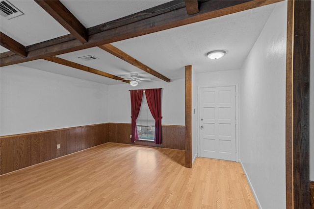 interior space featuring beamed ceiling, ceiling fan, light wood-type flooring, and wood walls