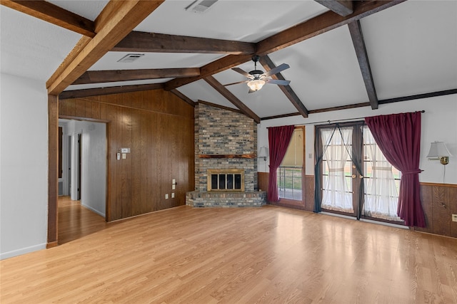 unfurnished living room featuring wood walls, lofted ceiling with beams, light wood-type flooring, ceiling fan, and a fireplace