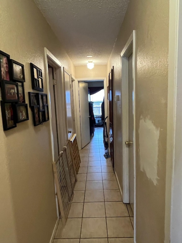 corridor featuring baseboards, a textured ceiling, light tile patterned flooring, and a textured wall