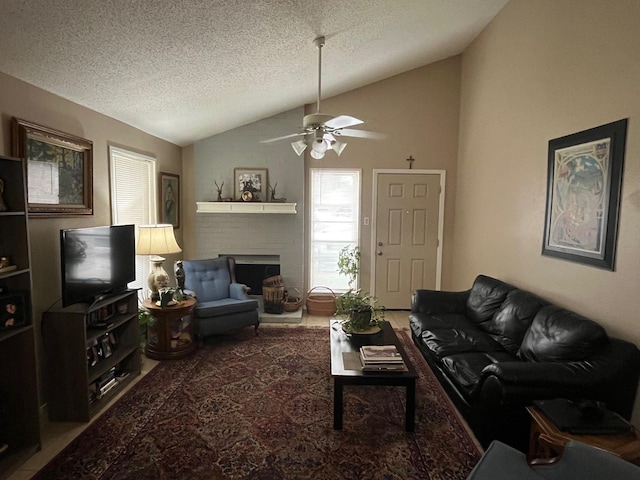 living area featuring a textured ceiling, a brick fireplace, ceiling fan, and vaulted ceiling