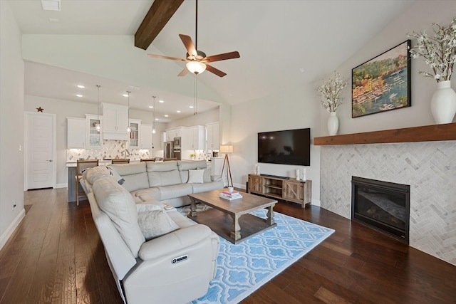 living room with vaulted ceiling with beams, dark wood-type flooring, a tile fireplace, and ceiling fan