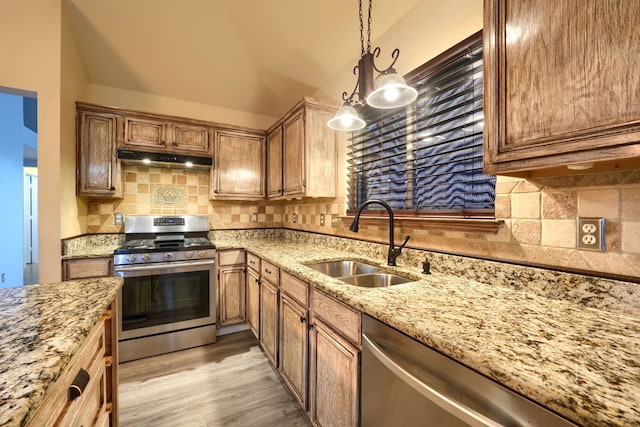 kitchen featuring pendant lighting, sink, decorative backsplash, stainless steel appliances, and light wood-type flooring