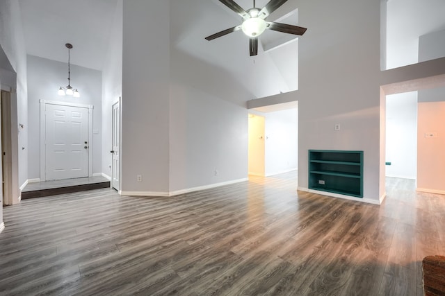 unfurnished living room with dark hardwood / wood-style flooring, a towering ceiling, and ceiling fan with notable chandelier