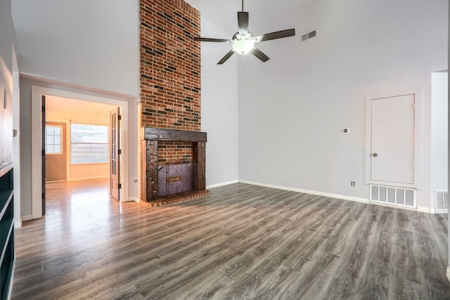 unfurnished living room with ceiling fan, wood-type flooring, a brick fireplace, and a high ceiling