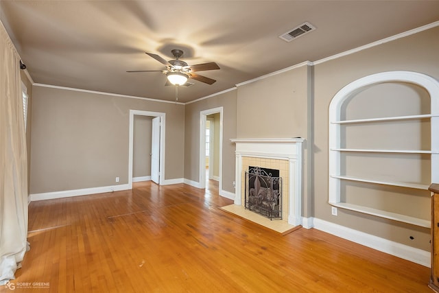 unfurnished living room with crown molding, a tile fireplace, built in features, hardwood / wood-style flooring, and ceiling fan