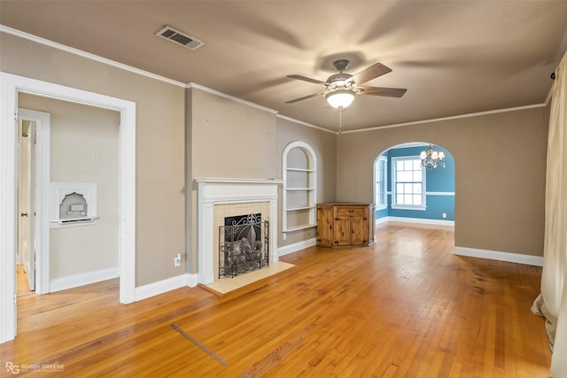 unfurnished living room featuring built in features, ceiling fan, a fireplace, ornamental molding, and wood-type flooring