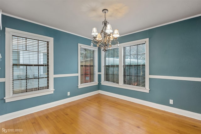 empty room featuring an inviting chandelier, hardwood / wood-style floors, crown molding, and a healthy amount of sunlight