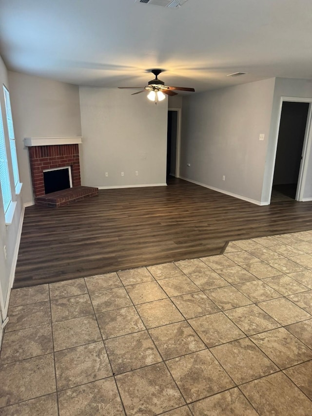 unfurnished living room featuring a brick fireplace, dark wood-type flooring, and ceiling fan