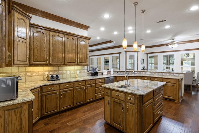 kitchen with dark hardwood / wood-style flooring, hanging light fixtures, ornamental molding, a kitchen island with sink, and kitchen peninsula