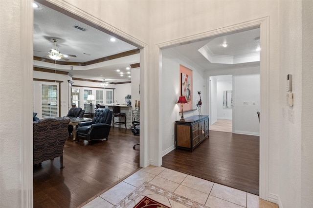 entryway with ceiling fan, ornamental molding, a raised ceiling, and light hardwood / wood-style flooring