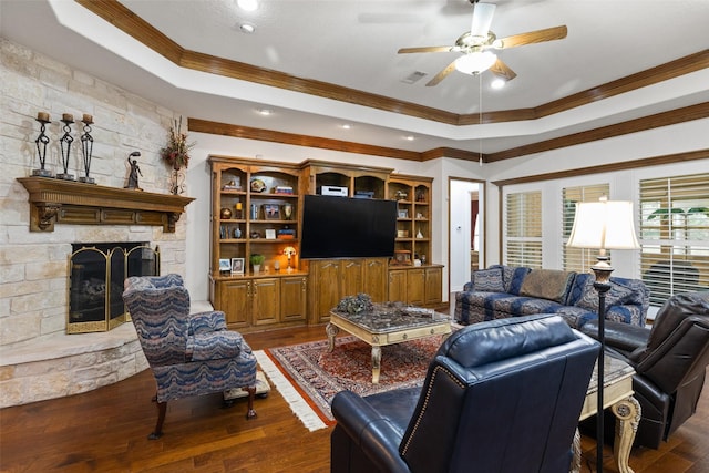 living room with a fireplace, dark hardwood / wood-style flooring, ceiling fan, a tray ceiling, and crown molding