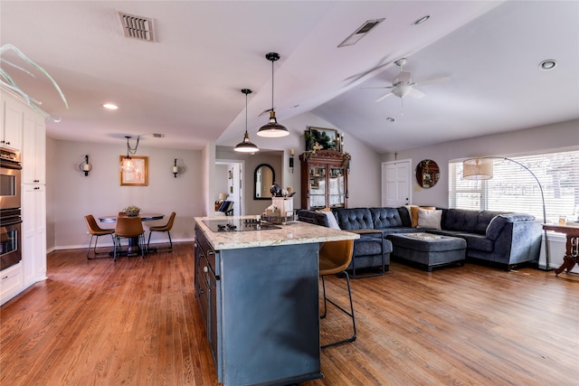 kitchen featuring light stone counters, hanging light fixtures, a center island with sink, hardwood / wood-style floors, and white cabinets