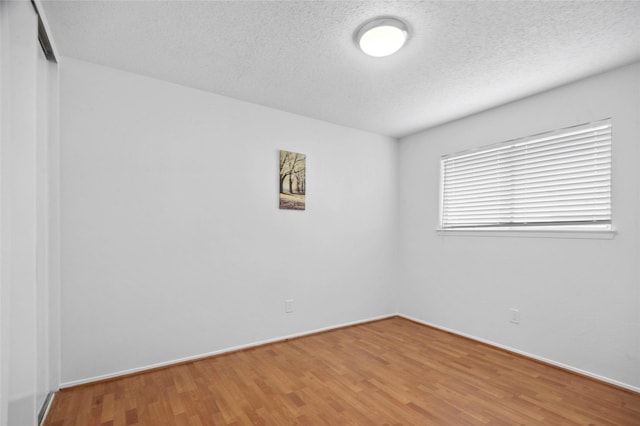 spare room with a textured ceiling, wood finished floors, and baseboards