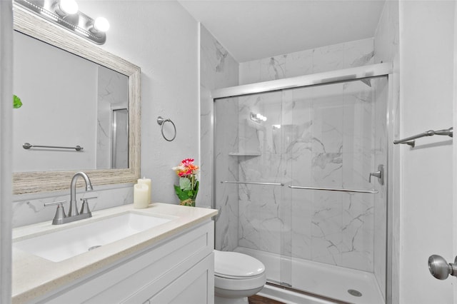 bathroom with a textured wall, toilet, vanity, and a marble finish shower