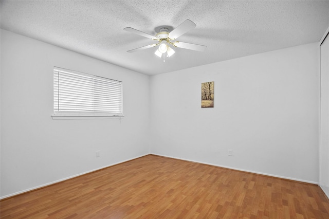 spare room featuring light wood-type flooring, a textured ceiling, baseboards, and a ceiling fan