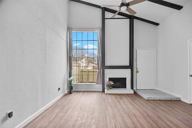 unfurnished living room featuring high vaulted ceiling, a fireplace, ceiling fan, light hardwood / wood-style floors, and beam ceiling