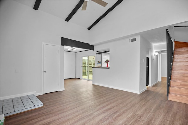 unfurnished room featuring high vaulted ceiling, wood finished floors, visible vents, and stairs