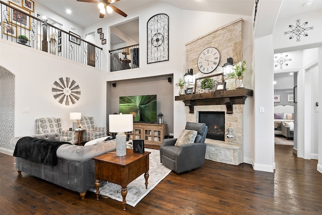 living room with dark hardwood / wood-style flooring, a fireplace, ceiling fan, and a high ceiling