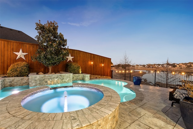 pool at dusk with a patio area, pool water feature, and an in ground hot tub