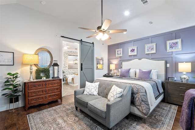 bedroom featuring vaulted ceiling, dark hardwood / wood-style flooring, ceiling fan, a barn door, and ensuite bath