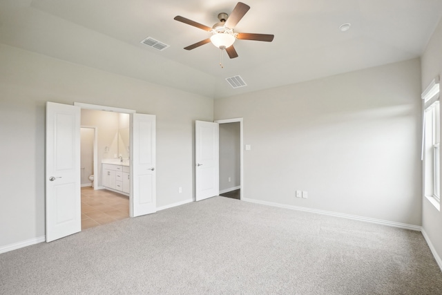 unfurnished bedroom featuring multiple windows, connected bathroom, light colored carpet, and ceiling fan