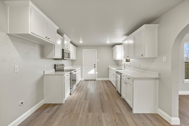 kitchen with appliances with stainless steel finishes, sink, white cabinets, and light hardwood / wood-style flooring