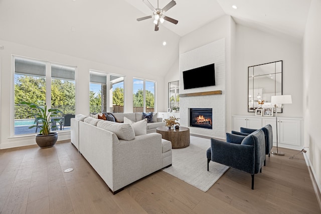 living room with ceiling fan, high vaulted ceiling, light hardwood / wood-style floors, and a brick fireplace