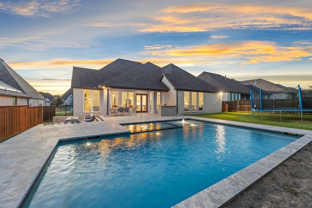 pool at dusk featuring a trampoline, a patio, and an outdoor fire pit