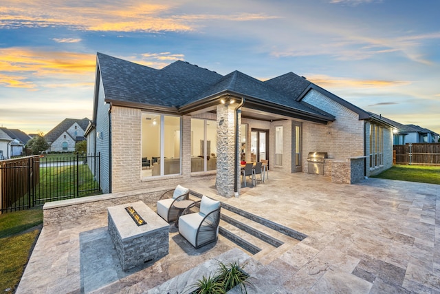 back house at dusk with a fire pit, an outdoor kitchen, and a patio area