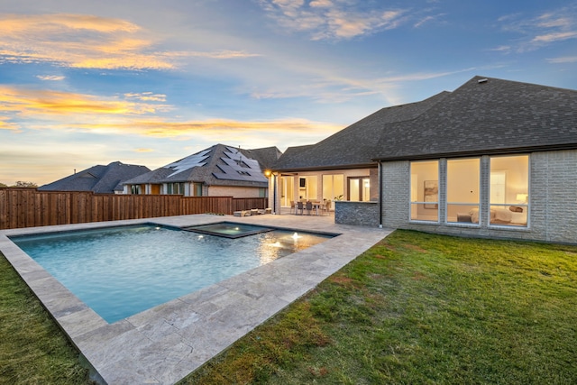 pool at dusk featuring an in ground hot tub, a patio, and a lawn