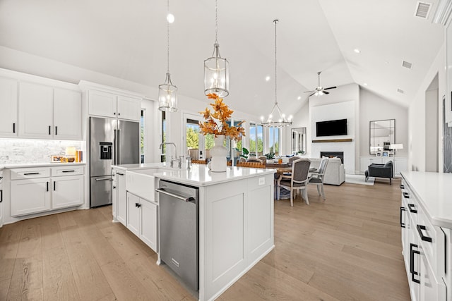 kitchen with pendant lighting, sink, appliances with stainless steel finishes, a kitchen island with sink, and white cabinets