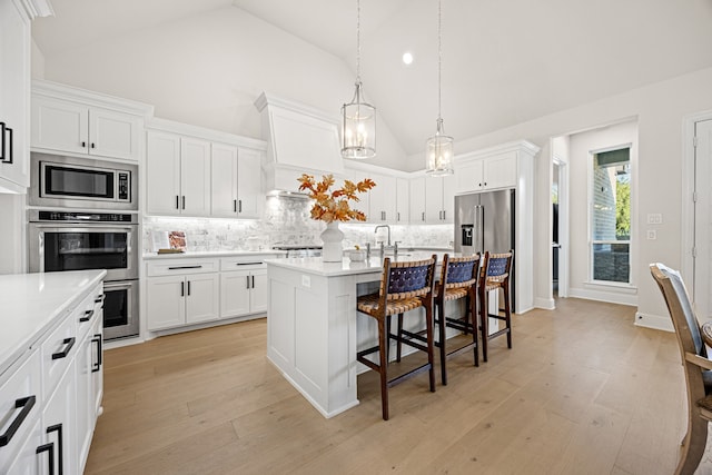 kitchen featuring a breakfast bar, white cabinets, a kitchen island with sink, stainless steel appliances, and light hardwood / wood-style flooring