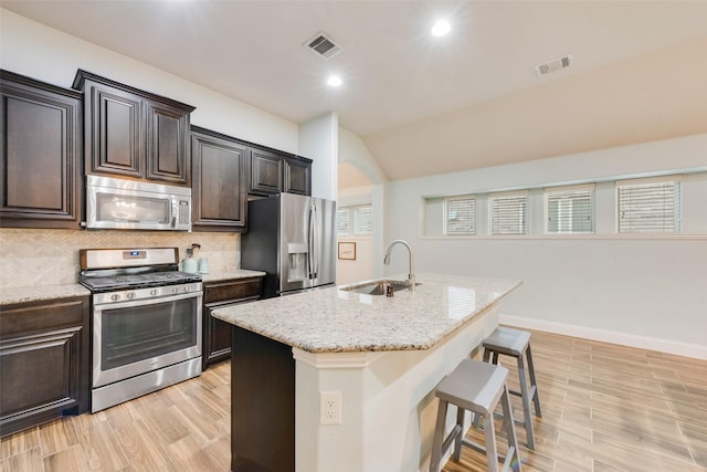 kitchen with sink, a breakfast bar, appliances with stainless steel finishes, backsplash, and a center island with sink