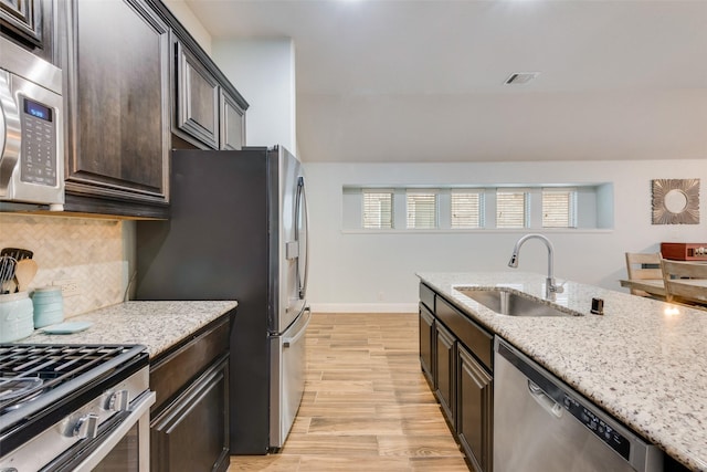 kitchen with appliances with stainless steel finishes, tasteful backsplash, sink, dark brown cabinetry, and light hardwood / wood-style floors