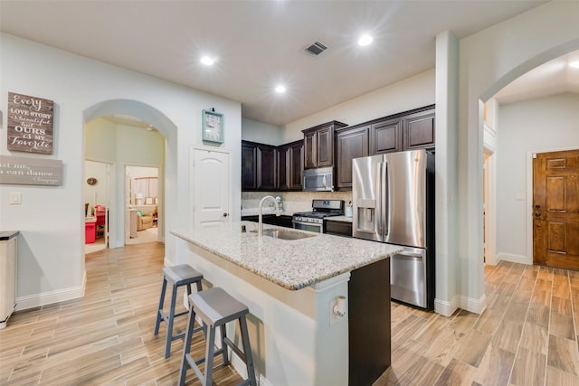 kitchen with sink, a kitchen bar, a kitchen island with sink, stainless steel appliances, and light stone countertops