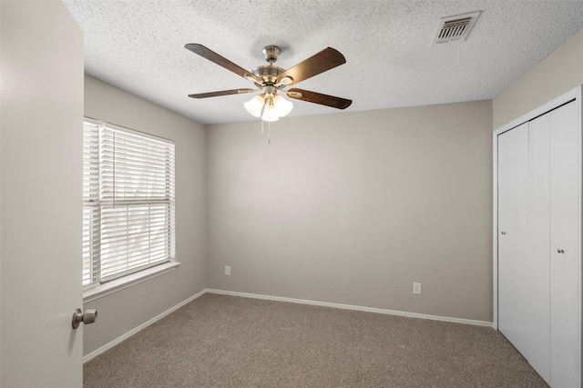 unfurnished bedroom with ceiling fan, carpet, a textured ceiling, and a closet