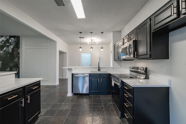 kitchen with appliances with stainless steel finishes, decorative light fixtures, sink, kitchen peninsula, and a textured ceiling