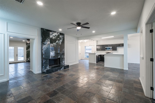 unfurnished living room featuring french doors, ceiling fan, a premium fireplace, and a textured ceiling