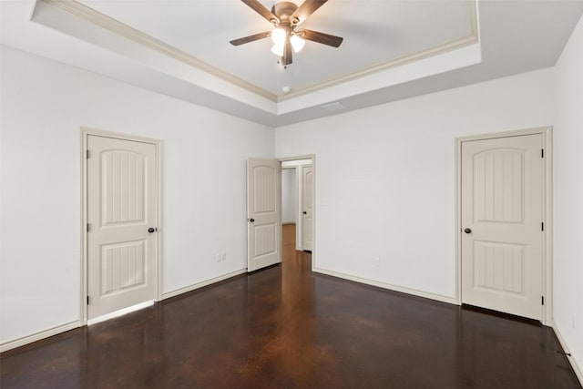 empty room with finished concrete flooring, baseboards, a raised ceiling, a ceiling fan, and crown molding