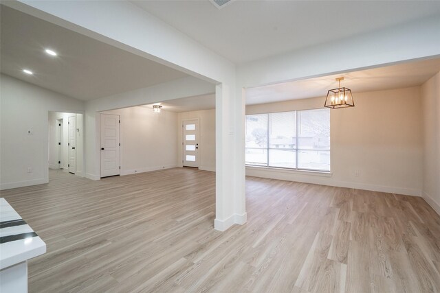 unfurnished living room featuring a notable chandelier and light wood-type flooring